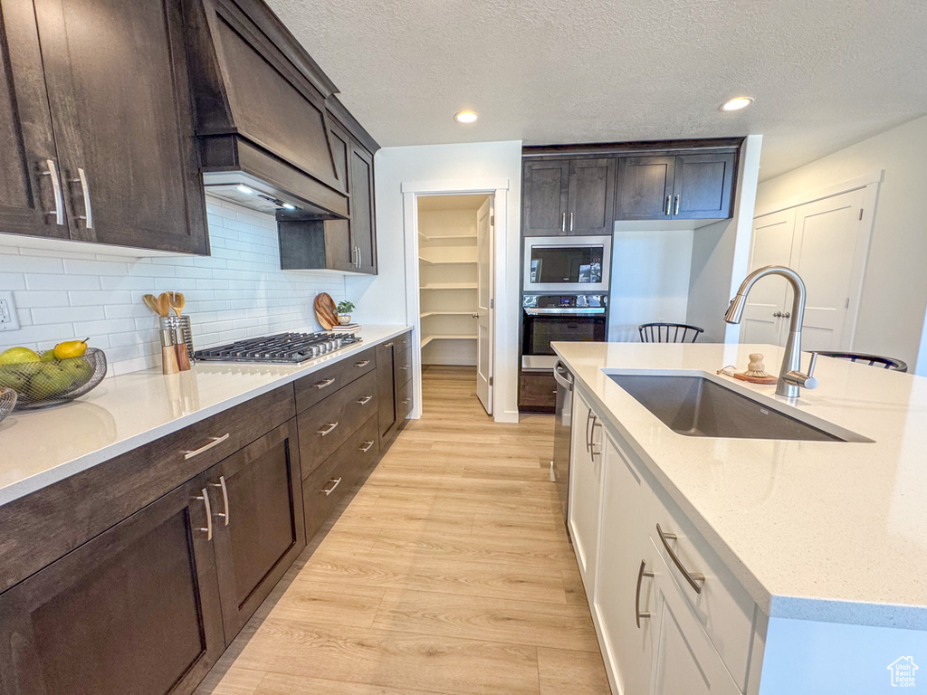 Kitchen with appliances with stainless steel finishes, light wood-style floors, dark brown cabinets, backsplash, and a textured ceiling