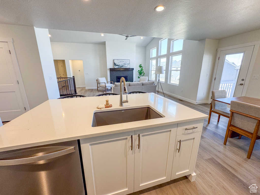 Kitchen with dishwasher, light wood-type flooring, a fireplace, light countertops, and a textured ceiling