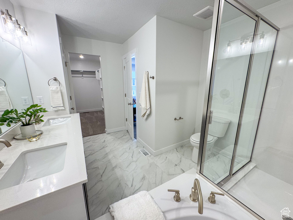 Full bathroom with double vanity, marble finish flooring, a walk in closet, a shower stall, and a textured ceiling
