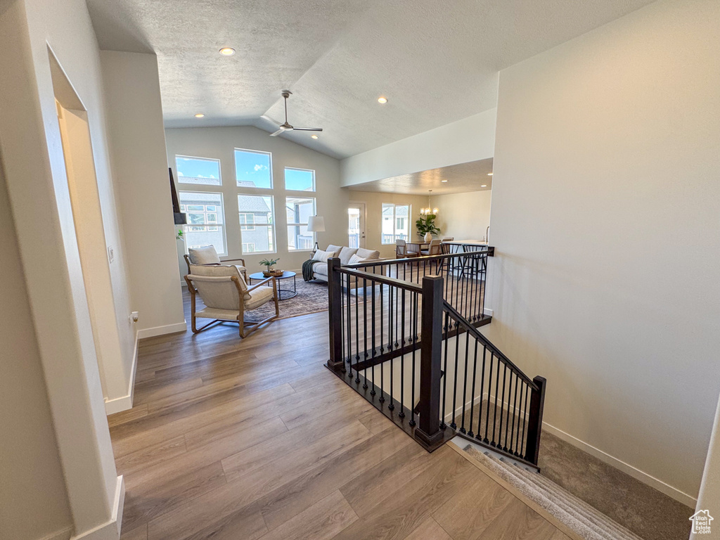 Hallway featuring an upstairs landing, vaulted ceiling, wood finished floors, a textured ceiling, and a chandelier