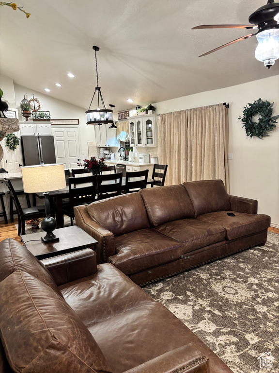 Living room with ceiling fan with notable chandelier, wood-type flooring, and lofted ceiling