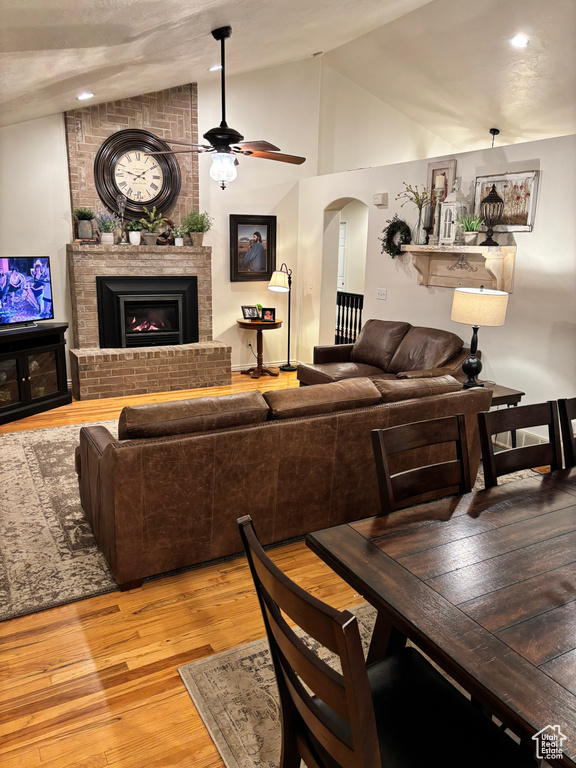 Living room with hardwood / wood-style floors, vaulted ceiling, ceiling fan, and a brick fireplace