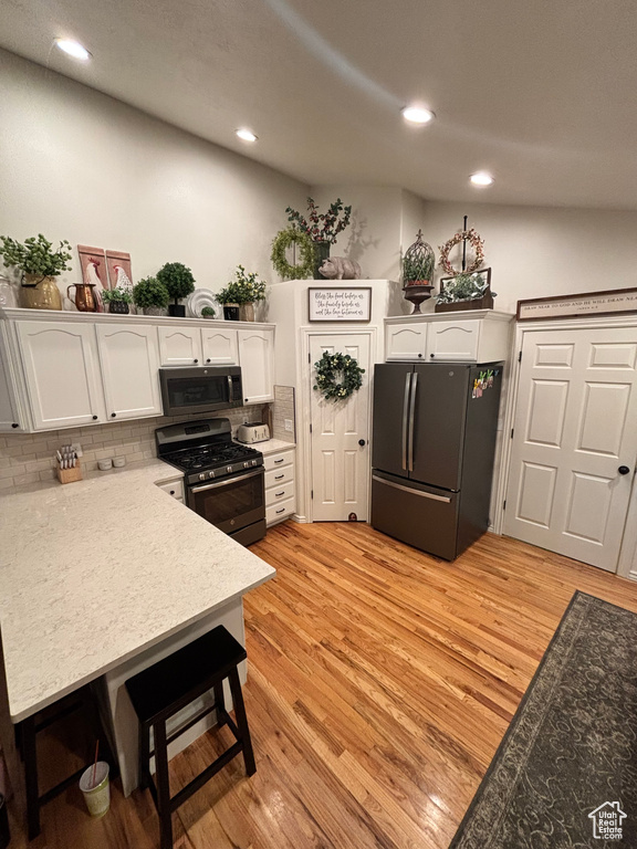 Kitchen with white cabinets, decorative backsplash, light wood-type flooring, and stainless steel appliances