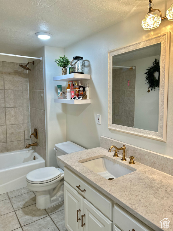 Full bathroom with vanity, tile patterned floors, tiled shower / bath combo, toilet, and a textured ceiling