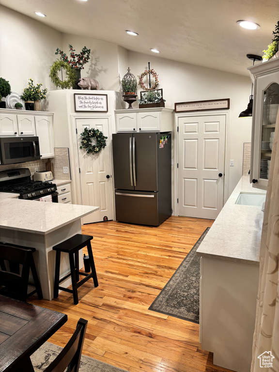 Kitchen featuring decorative backsplash, light hardwood / wood-style floors, white cabinetry, and stainless steel appliances