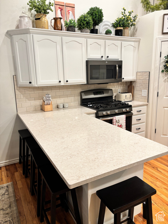 Kitchen featuring a kitchen bar, white cabinetry, kitchen peninsula, and appliances with stainless steel finishes