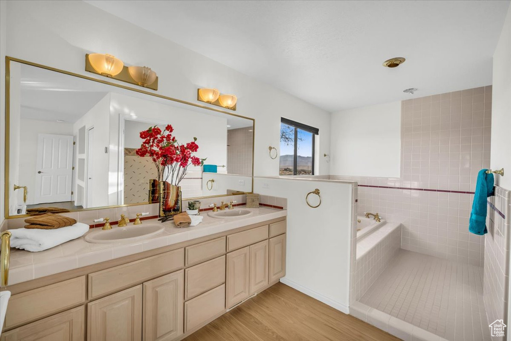 Bathroom featuring wood-type flooring, vanity, tile walls, and tiled tub