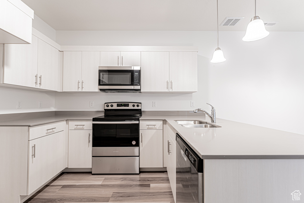 Kitchen with appliances with stainless steel finishes, a sink, a peninsula, light countertops, and decorative light fixtures