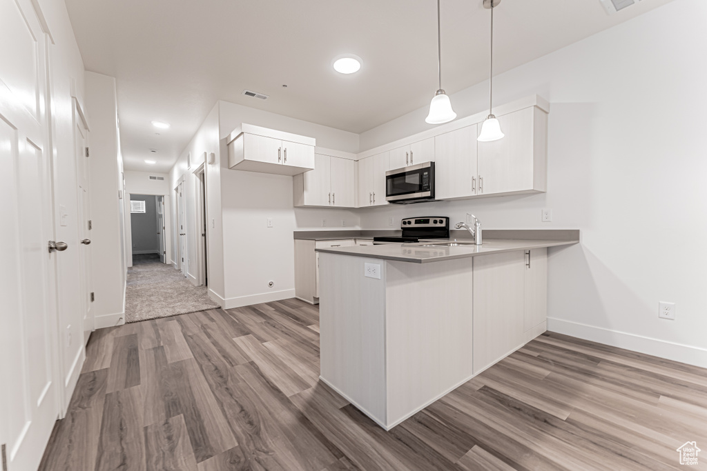 Kitchen featuring stainless steel appliances, a peninsula, a sink, light wood-type flooring, and white cabinets