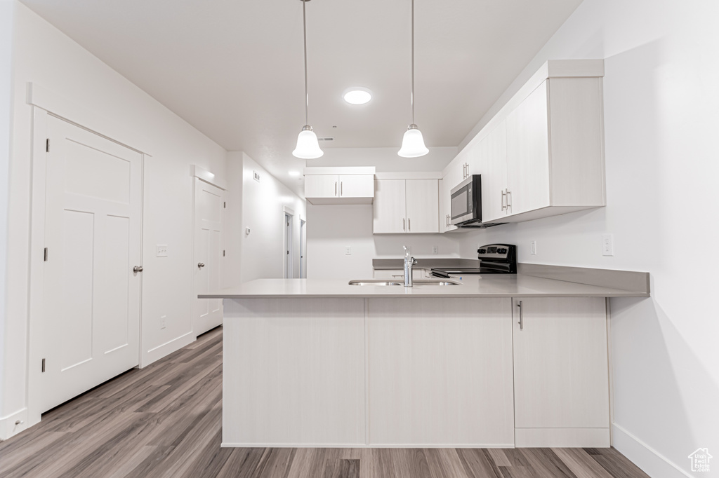 Kitchen featuring stainless steel appliances, a sink, a peninsula, baseboards, and light wood-style flooring