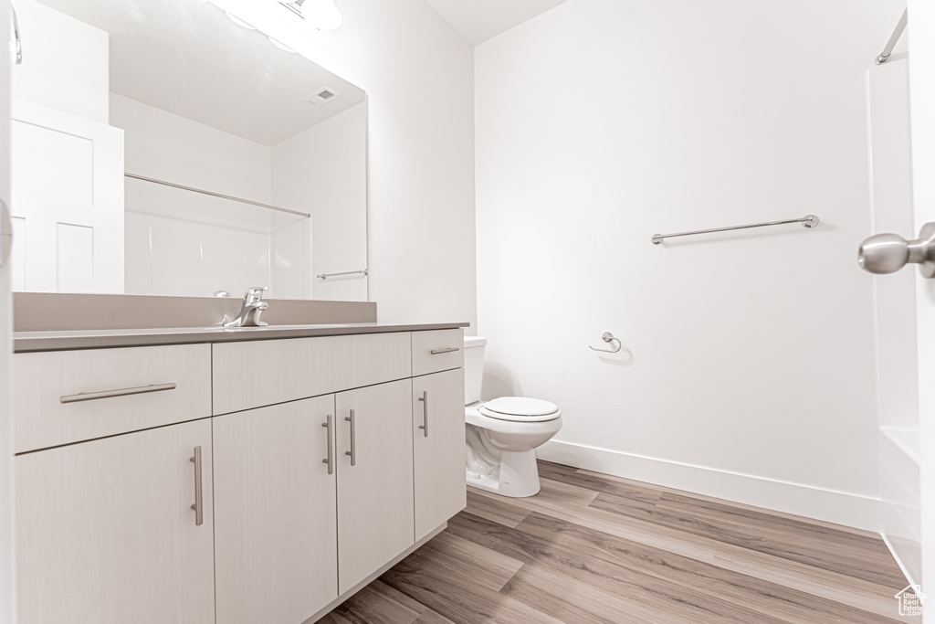 Bathroom with vanity, toilet, wood finished floors, baseboards, and shower / washtub combination