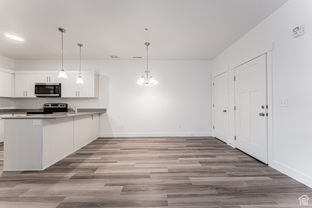 Kitchen featuring stainless steel microwave, electric range oven, baseboards, and white cabinetry