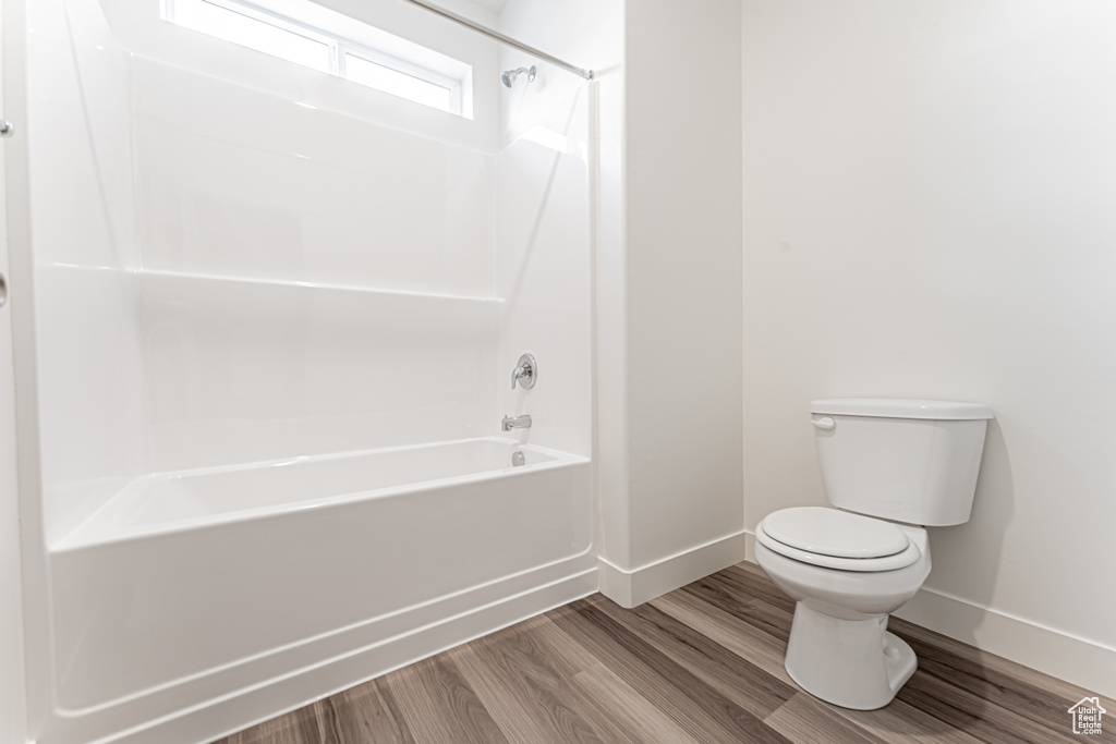 Bathroom with toilet, bathing tub / shower combination, baseboards, and wood finished floors