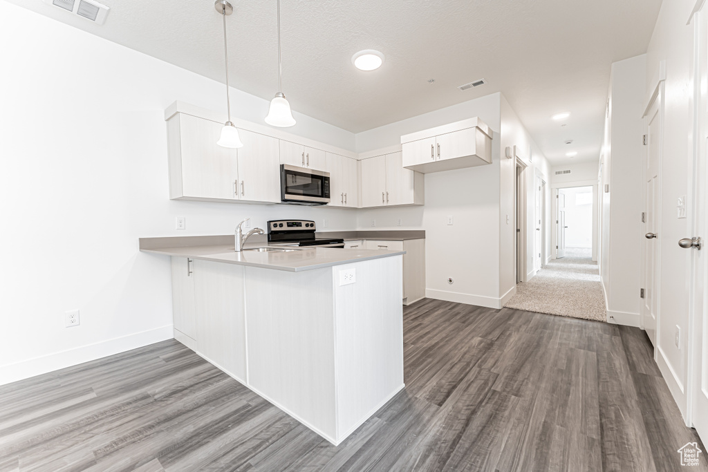 Kitchen with appliances with stainless steel finishes, a peninsula, wood finished floors, baseboards, and white cabinetry