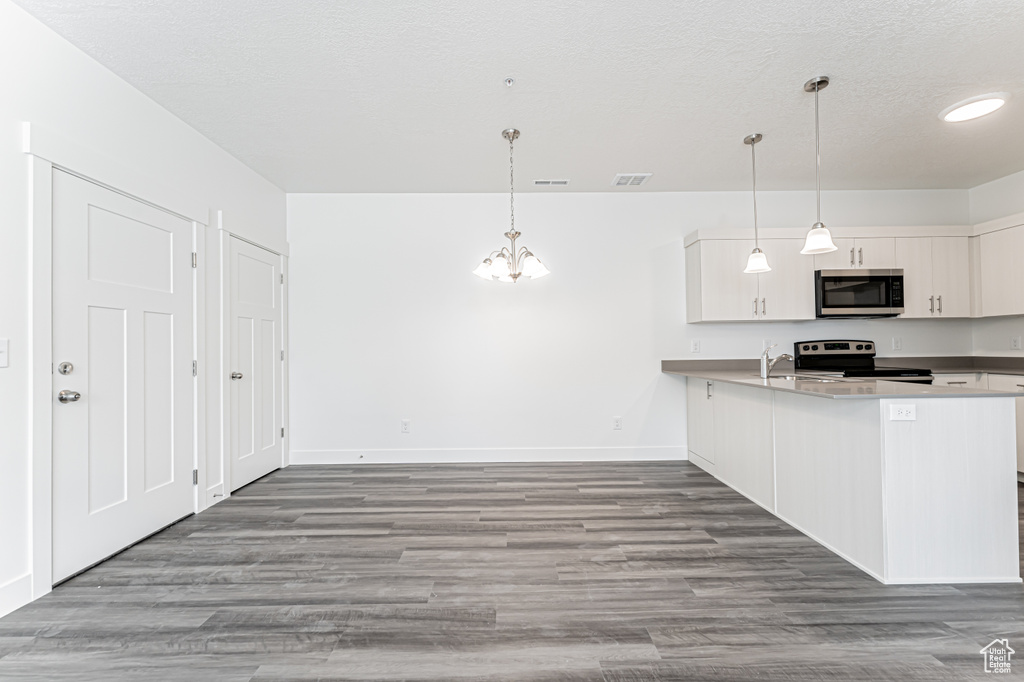 Kitchen featuring appliances with stainless steel finishes, a chandelier, wood finished floors, baseboards, and a peninsula