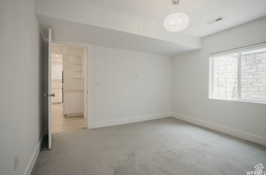 Empty room featuring light carpet and an inviting chandelier