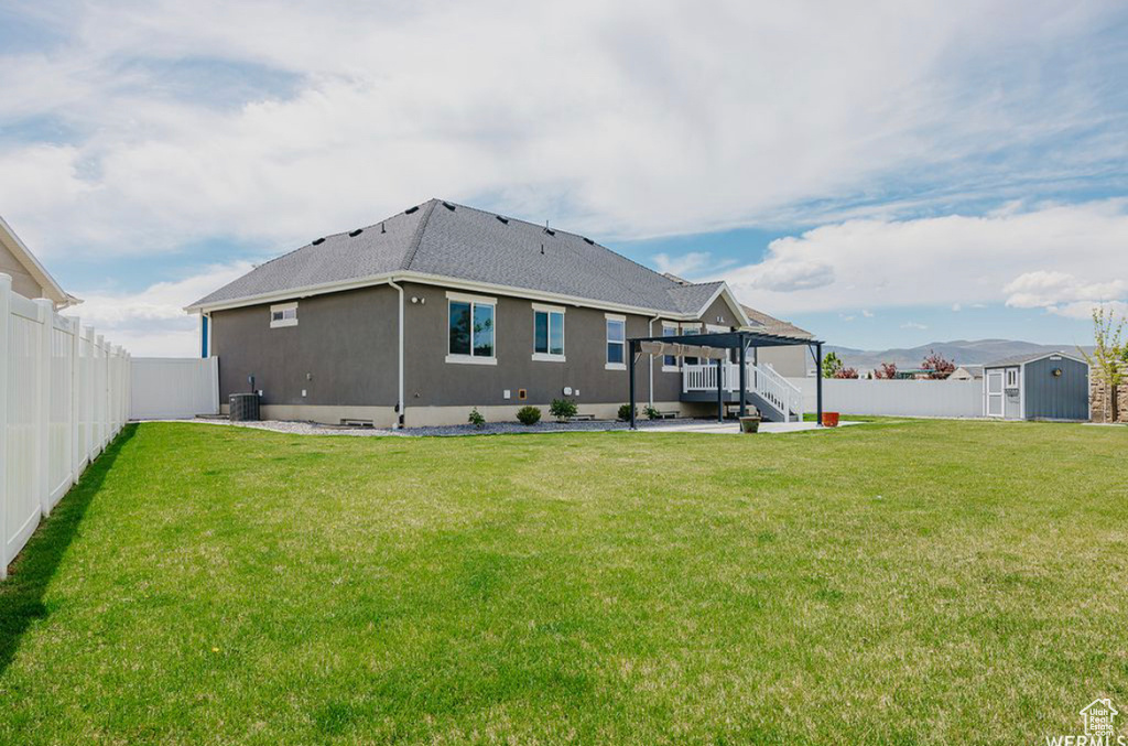 Rear view of house featuring a pergola, central AC, a storage unit, and a lawn