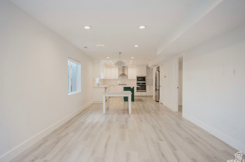 Kitchen with decorative backsplash, light wood-type flooring, stainless steel appliances, wall chimney range hood, and white cabinetry