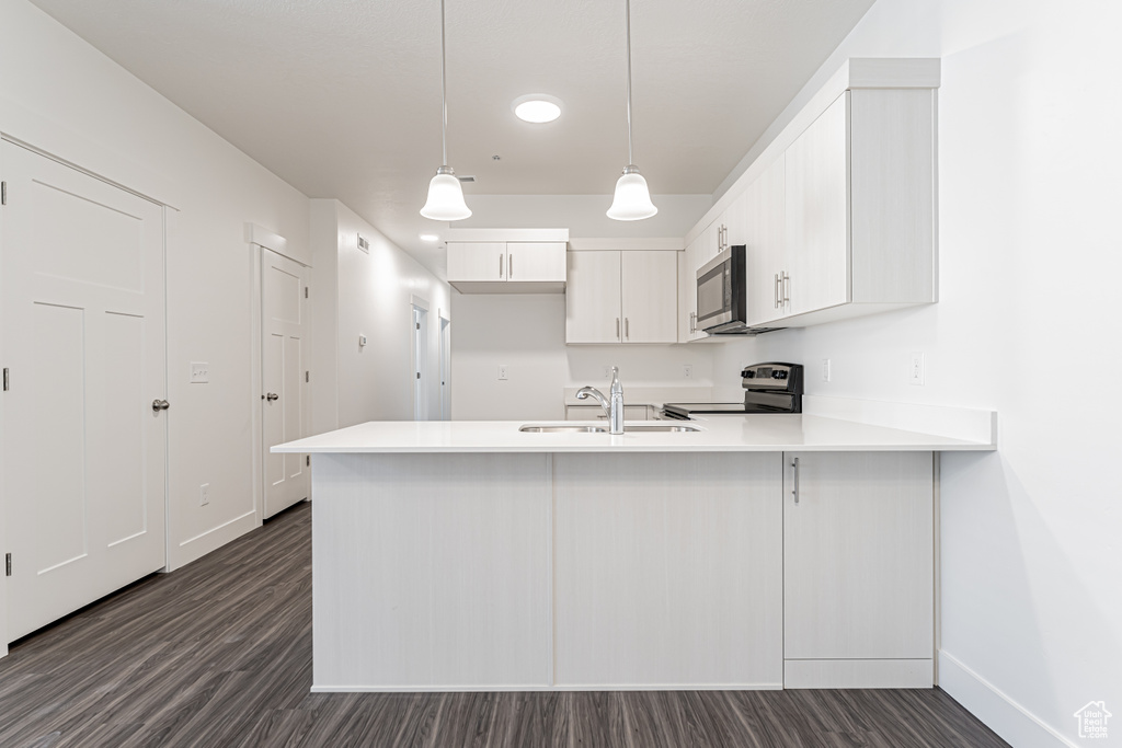 Kitchen featuring appliances with stainless steel finishes, a sink, a peninsula, baseboards, and dark wood-type flooring