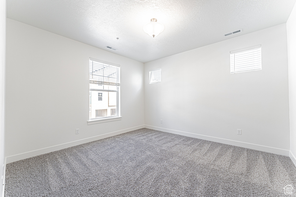 Empty room with carpet, baseboards, and a textured ceiling