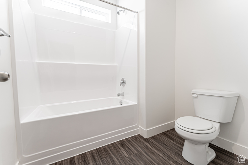 Bathroom with baseboards, toilet, wood finished floors, and shower / tub combination