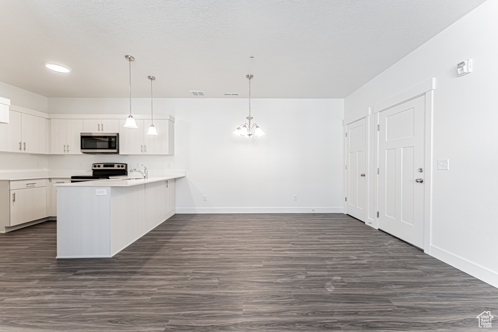 Kitchen with appliances with stainless steel finishes, a peninsula, a chandelier, a sink, and white cabinetry