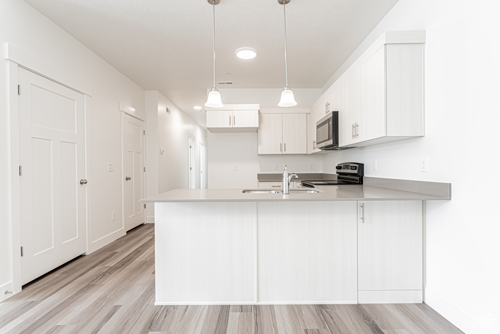 Kitchen featuring appliances with stainless steel finishes, a sink, a peninsula, light wood-style floors, and light countertops