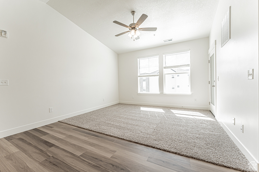 Unfurnished room with ceiling fan, wood finished floors, vaulted ceiling, a textured ceiling, and baseboards
