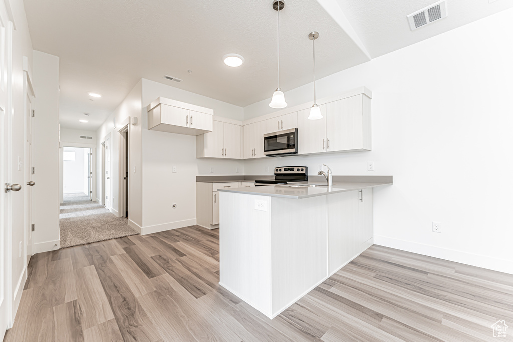Kitchen with appliances with stainless steel finishes, a peninsula, light wood-type flooring, a sink, and white cabinets