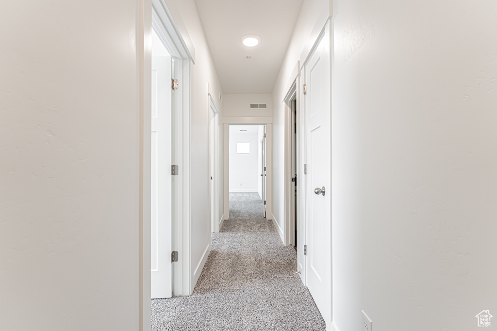 Hallway with light colored carpet and baseboards