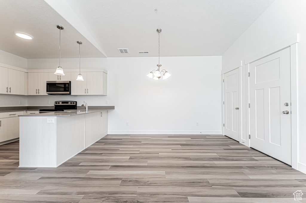 Kitchen featuring stainless steel appliances, a peninsula, light wood finished floors, hanging light fixtures, and white cabinets