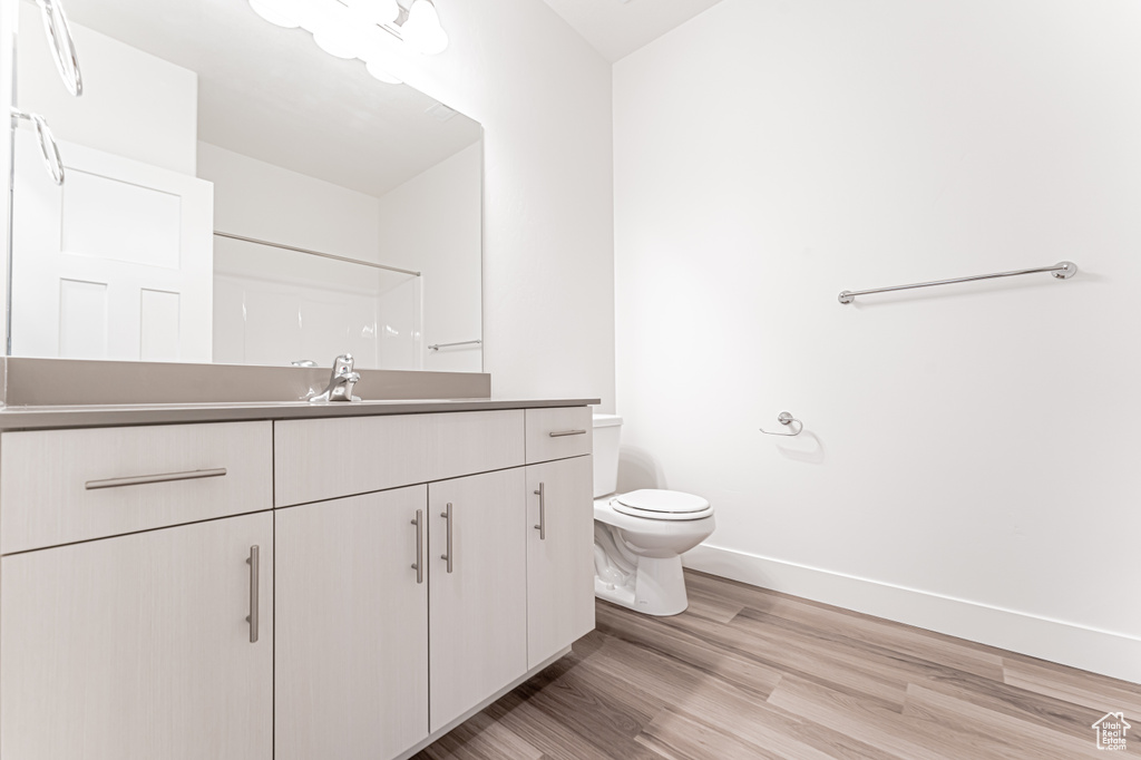 Full bath featuring vanity, toilet, baseboards, wood finished floors, and a shower