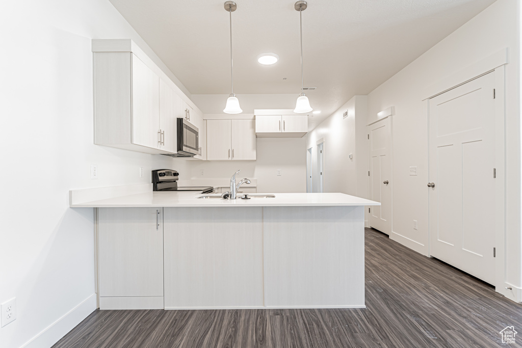 Kitchen featuring appliances with stainless steel finishes, a peninsula, dark wood-type flooring, a sink, and light countertops