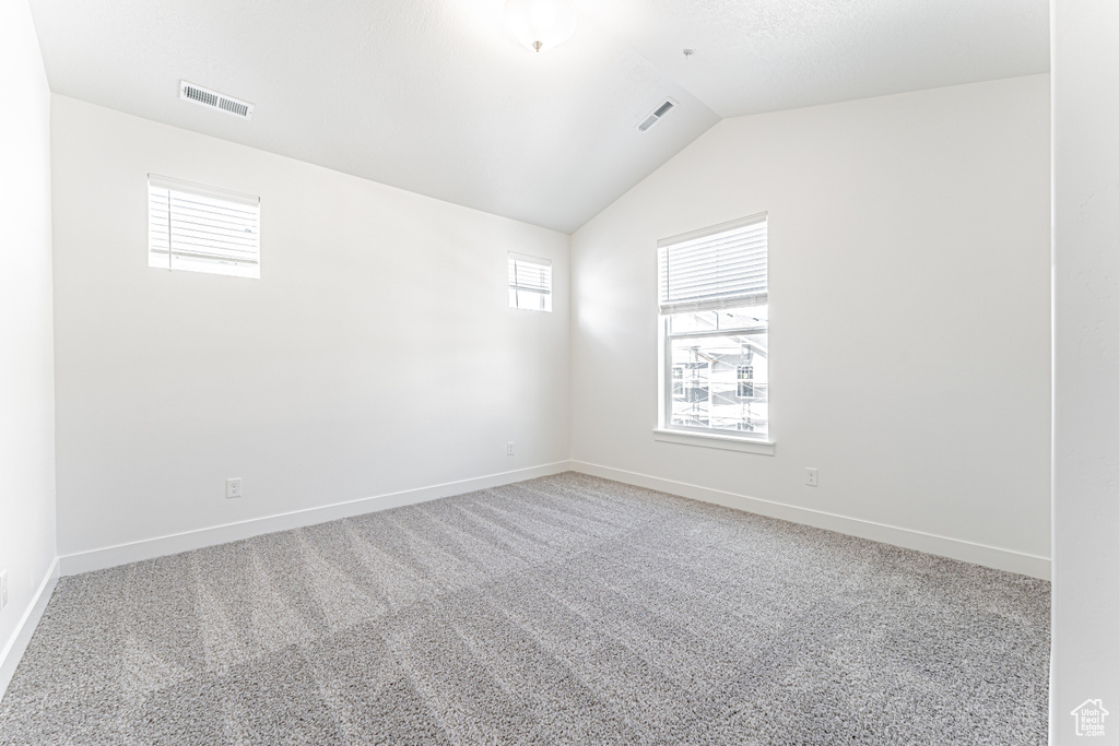 Empty room featuring baseboards, light colored carpet, and lofted ceiling