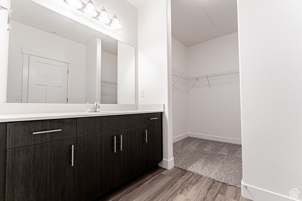 Bathroom featuring vanity, wood finished floors, a walk in closet, and baseboards
