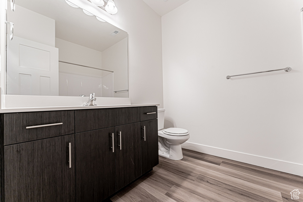 Bathroom with vanity, wood finished floors, toilet, baseboards, and a shower