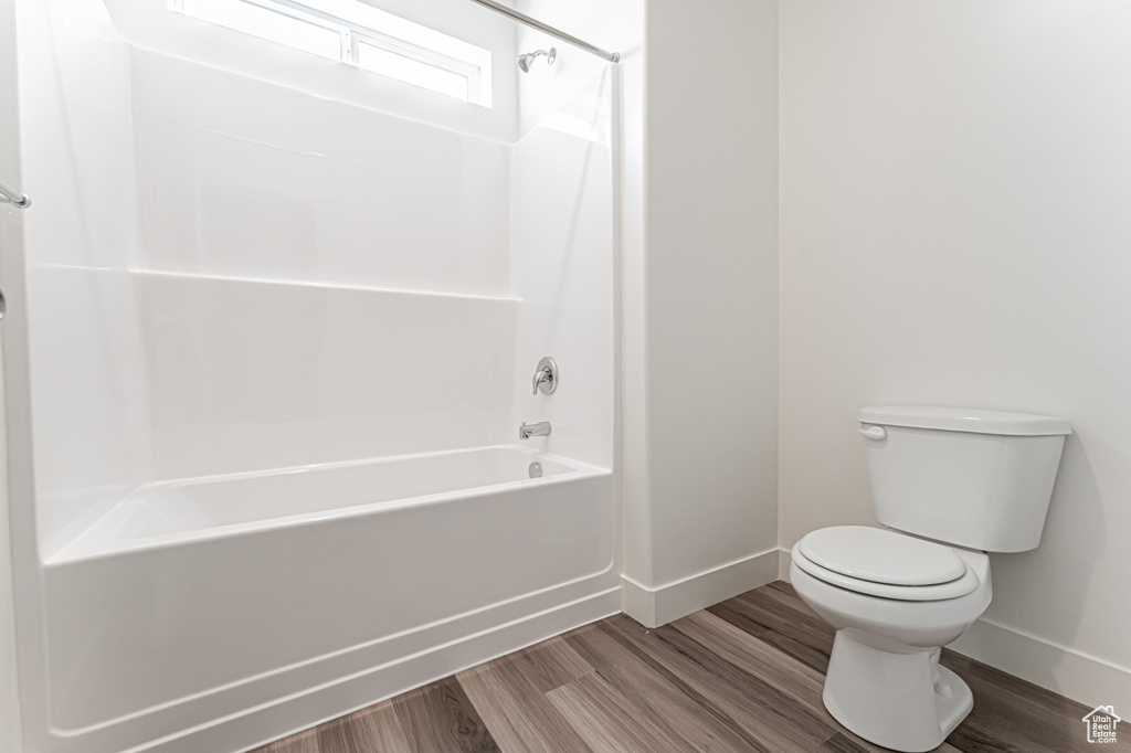 Full bathroom featuring baseboards, toilet, wood finished floors, and bathing tub / shower combination