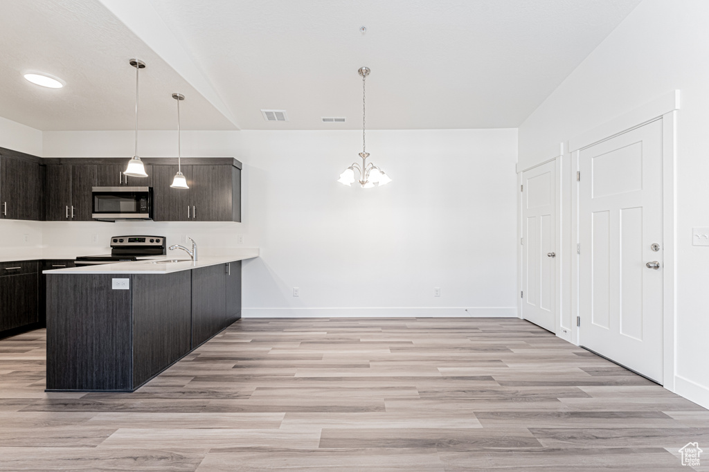 Kitchen featuring appliances with stainless steel finishes, a chandelier, light wood-style flooring, and a peninsula