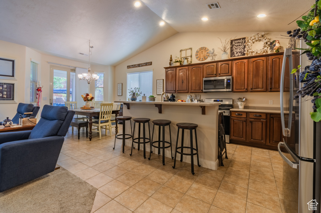 Kitchen featuring an island with sink, pendant lighting, vaulted ceiling, a breakfast bar area, and appliances with stainless steel finishes