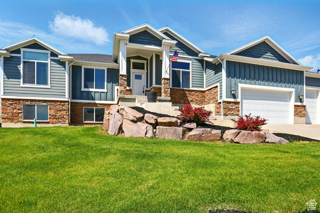 View of front of house featuring stone siding, board and batten siding, a front lawn, and concrete driveway