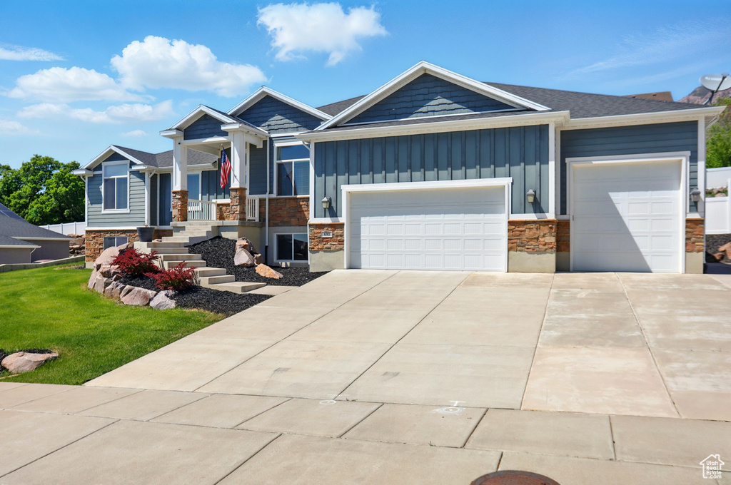 View of front facade with board and batten siding, stone siding, an attached garage, driveway, and a porch