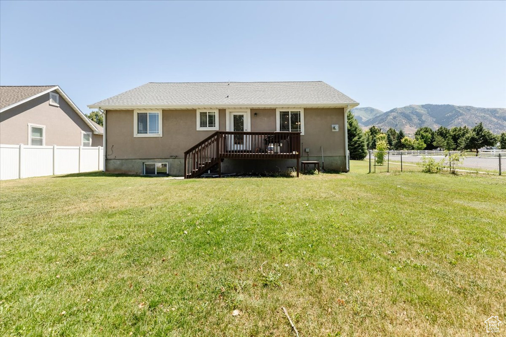 Back of property with a deck with mountain view and a lawn