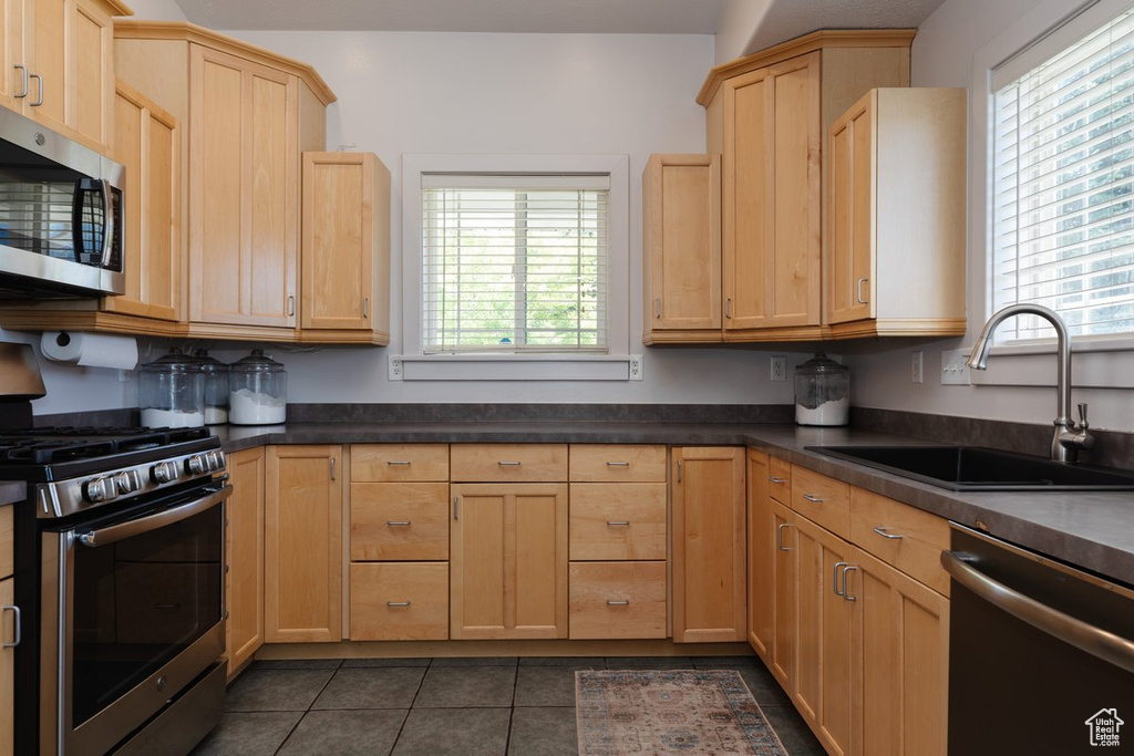 Kitchen with light brown cabinetry, sink, dark tile patterned flooring, and stainless steel appliances