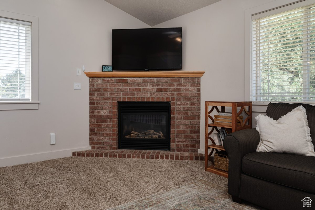 Carpeted living room featuring plenty of natural light, a brick fireplace, and vaulted ceiling