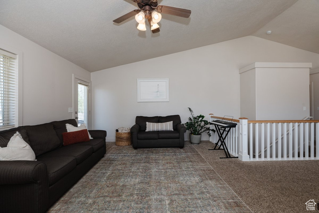 Carpeted living room featuring lofted ceiling, ceiling fan, and plenty of natural light