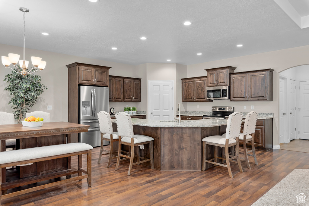 Kitchen with light stone countertops, dark hardwood / wood-style flooring, stainless steel appliances, pendant lighting, and a center island with sink