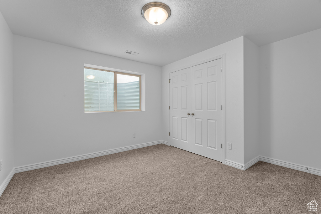 Unfurnished bedroom featuring carpet flooring, a textured ceiling, and a closet