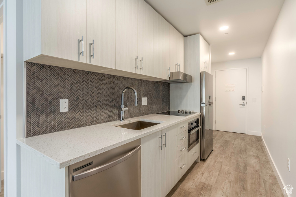 Kitchen featuring appliances with stainless steel finishes, backsplash, light stone counters, sink, and light hardwood / wood-style floors