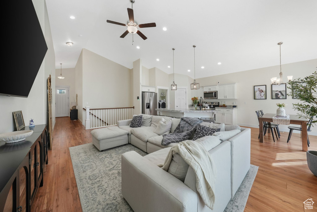 Living room featuring light wood-type flooring, ceiling fan with notable chandelier, and high vaulted ceiling