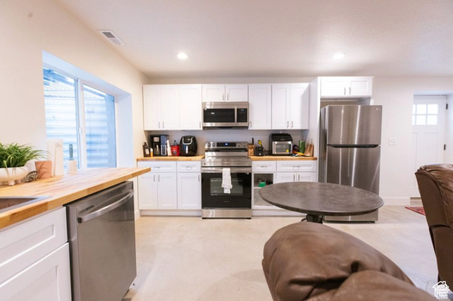Kitchen featuring wooden counters, appliances with stainless steel finishes, and white cabinets